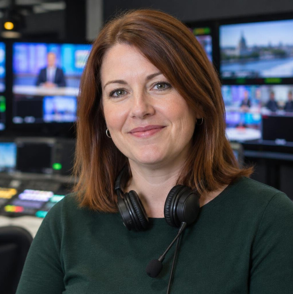 Portrait of a white British woman with shoulder length hair and headset around her neck